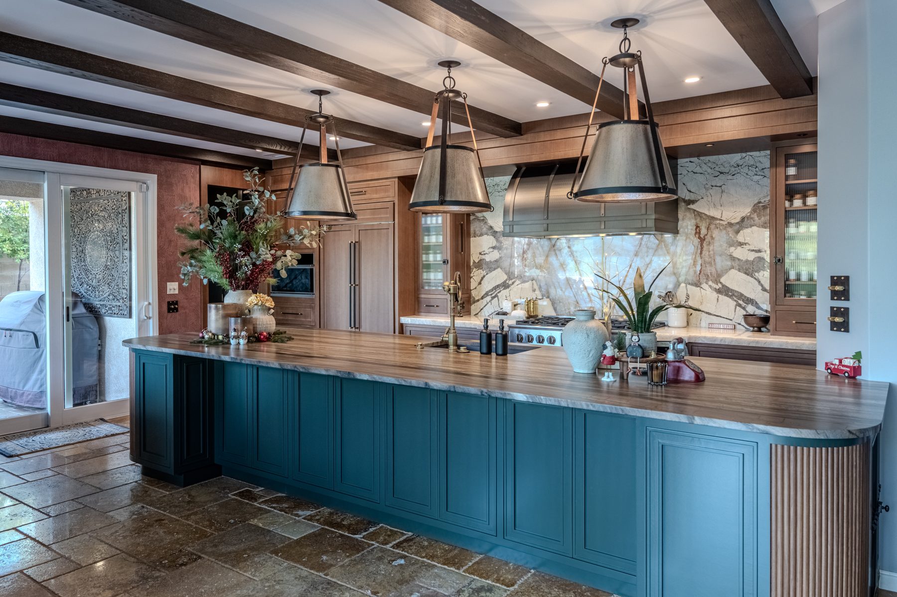 Custom blue kitchen island, wood cabinetry, ceiling beams, and full-height stone backsplash